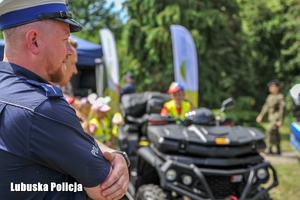 Policjanci na pikniku profilaktycznym, a w tle policyjny quad z dzieckiem.