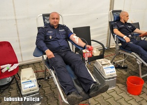 Mężczyzna w koszulce z napisem krew, a w tle policjanci podczas oddawania krwi.