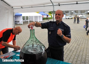 Policjant przelewa czerwony płyn do szklanego zbiornika.