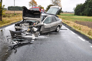 Miejsce wypadku drogowego - rozbity pojazd, a za nim pojazd straży pożarnej.