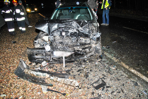 Miejsce wypadku drogowego - rozbity pojazd i pracujący na miejscu policjanci i strażacy.