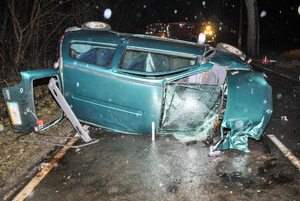 Miejsce wypadku drogowego - rozbity pojazd na boku i pracujący na miejscu policjanci.